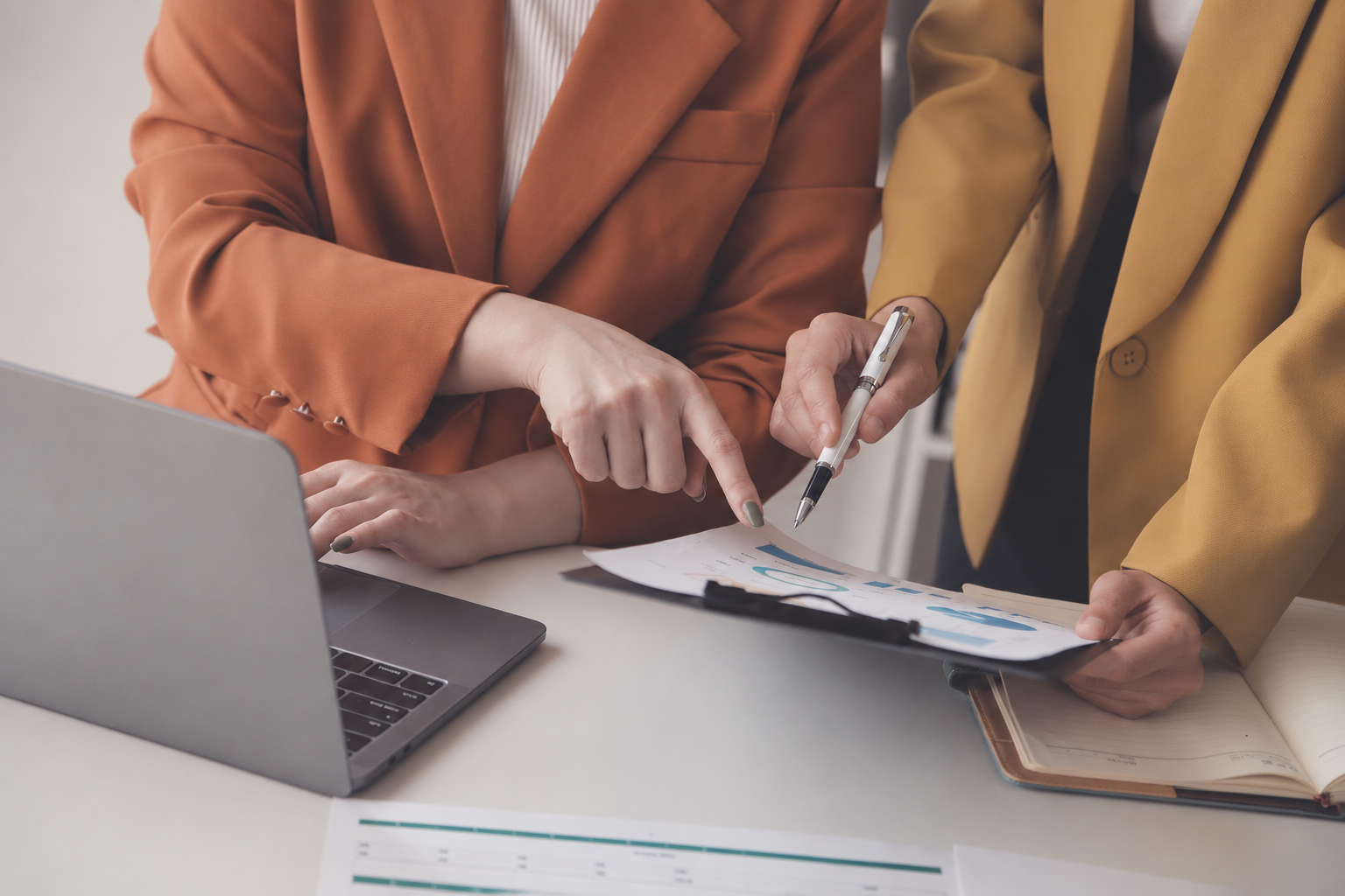 Two colleagues reviewing payroll reports beside a laptop